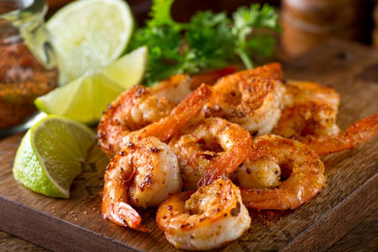 Grilled shrimp with lime wedges on wooden cutting board